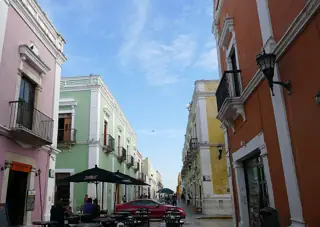 A narrow street lined with pink, green, yellow and orange facades and wrought-iron balconies.