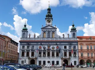 A pale blue Baroque town hall with three green-roofed towers and a central clock on a broad city square.