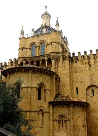 Golden stone apses with narrow arched windows stand below the cathedral tower and crenellated walls.