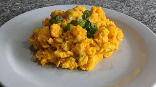 Yellow maize and scrambled egg with sliced green onions fill a plain white plate.