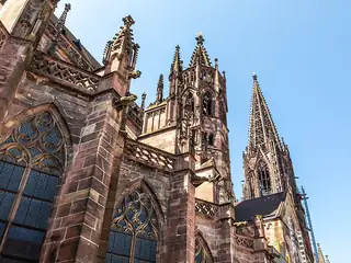 Low-angle view of reddish stone pinnacles, traceried windows and the openwork cathedral spire against blue sky.