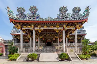 A richly carved clan-house front with tiled dragons along the sweeping roof and steps between potted shrubs.