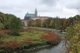 An autumn river bend with trees, the church’s twin spires and a long pale building beyond.
