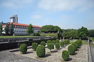 Rounded green topiary, stone terraces and balustrades below Vila Flor Palace, with a hotel tower behind.