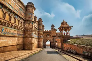 Sandstone palace walls decorated with blue tiles beside a sloping path and a carved pavilion.