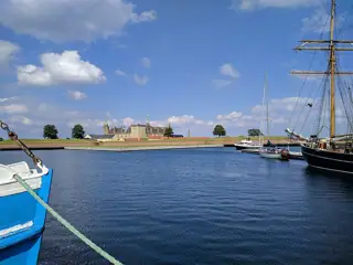 Blue harbor water and moored sailing vessels frame the distant towers and ramparts of Kronborg.