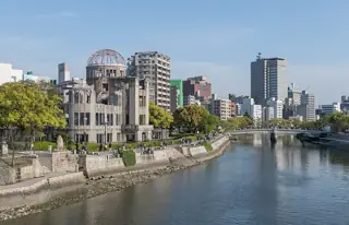 The preserved ruined dome and riverbank on the left, with the river, a bridge and city buildings extending into the distance.