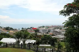 Palm trees and low-rise Honiara buildings below a blue coastal horizon.