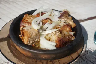 Browned meat topped with white onion strips in a black pan on a wooden serving board.