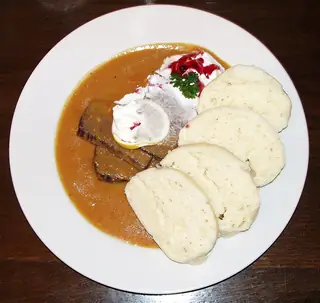 National food illustration of svíčková and sliced dumplings on a white plate, photographed in Prague.