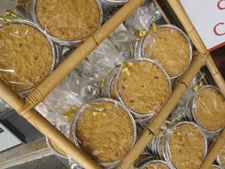 Round crumbly cakes wrapped in clear film and gold ribbons in foil trays on a diagonal rack.