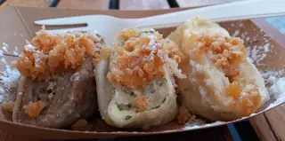 National illustration from Ljubljana: three sweet rolled dumpling portions in a plain cardboard tray with a plastic fork.