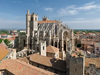 Stone buttresses and tall cathedral towers rise above terracotta roofs and a green courtyard.