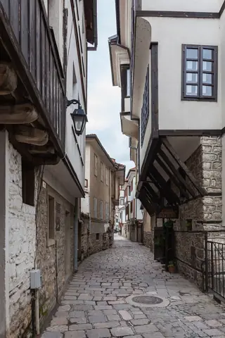 A narrow stone lane passes white overhanging houses with dark timber trim and closely spaced windows.