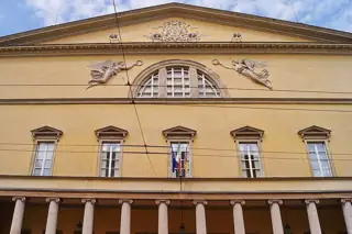 Yellow theatre facade with a triangular pediment, winged relief figures and columns cut by the lower source edge.