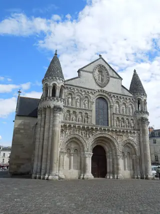 Carved stone church facade with a central patterned window, flanking turrets and a blue clouded sky.