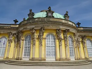 Yellow palace rotunda with carved stone figures, tall windows and a green dome against blue sky.