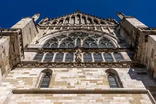 Gothic stone tracery, windows and fixed figures on the cathedral’s south facade against blue sky.