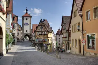 Quiet cobbled lanes split around a yellow timber-framed house between two town gates.