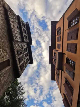 Timber-and-plaster projecting rooms and a neighboring modern facade frame a broad cloudy sky.