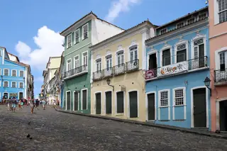 Green, yellow and blue historic facades line a cobbled square with visitors at the left.