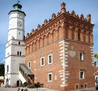 A brick town hall with an ornate attic, white clock tower and sundial under blue sky.