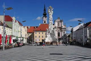The Trinity Column rises above Rathausplatz, with the Franciscan church and town facades behind.
