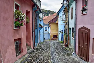 A quiet cobbled lane between yellow, green and ochre houses with flower pots and hanging signs.