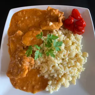 Regional food illustration, capture locality unstated: paprika chicken, dumplings, parsley and peppers on a plain white plate.
