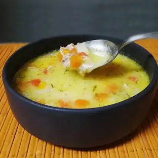 Creamy soup in a dark bowl with a spoon on a bamboo mat.
