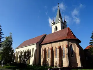 The stone apse and tall square tower of the Fortress Church rise beside grass and autumn trees.