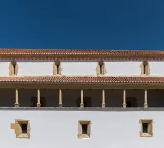 White church walls, a shaded stone-column loggia and tiled roofs below a deep blue sky.