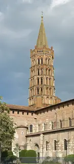 A tall brick bell tower rises above the nave and south transept of Saint-Sernin against a gray sky.