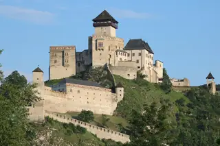 Castle towers, palaces and defensive walls on a rocky green hill beneath blue sky.