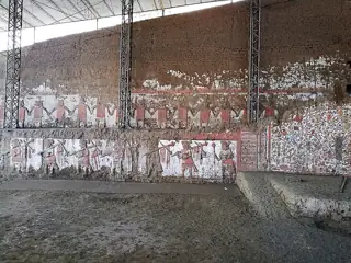 Weathered painted figures and geometric imagery remain on layered adobe walls beneath a protective roof at Huaca de la Luna.