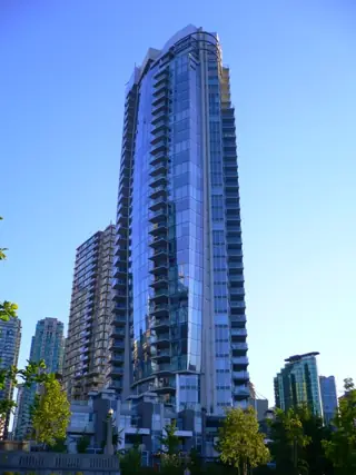 Slender blue-glass tower rising above trees and neighbouring buildings.