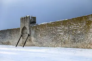 Snow-covered ground below a stone wall and saddle tower with dark support braces.