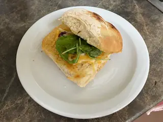 A floury white bread roll with cheese and greens on a plain white plate.