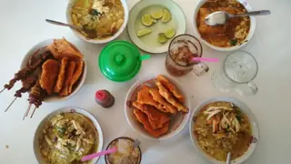 An overhead table of soup bowls, fried accompaniments, skewers, lime wedges and drinks.