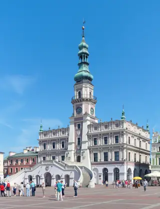 The pale mauve Town Hall with a tall copper-topped tower and curved stairs above visitors in the paved square.