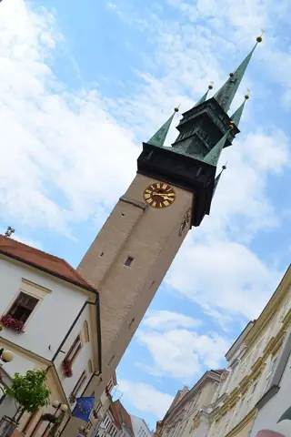 A sharply tilted view up a tall stone clock tower beneath bright clouds.